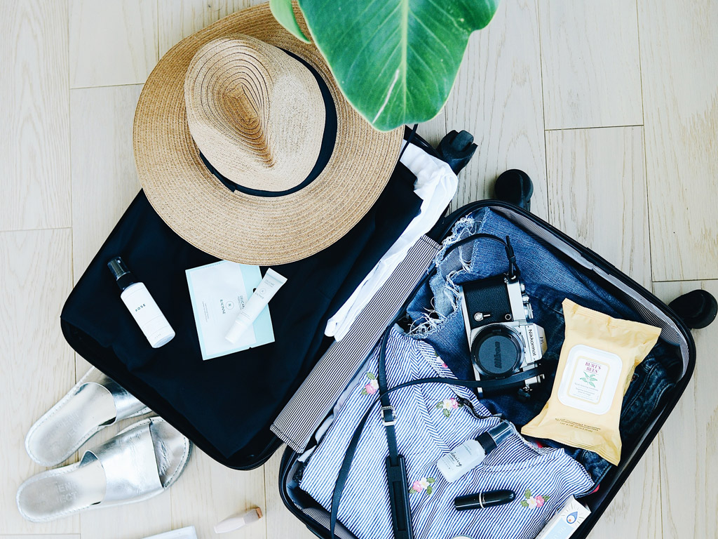 Open suitcase on floor showing clothes, a camera and other holiday items